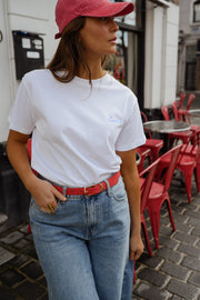 T-shirt à logo cœur dos porté par une femme, silhouette entière, casquette rouge, ceinture rouge, jean clair
