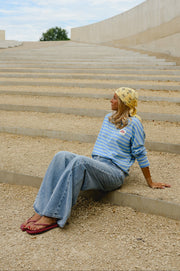 T-shirt rayé à patch porté par une femme, assise, sur des marches, de loin