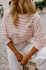T-shirt rayé à manches longues rose porté par une femme, vue de trois-quarts, pantalon blanc, mains jointes