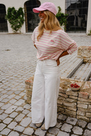 T-shirt rayé à manches longues rose porté par une femme, vue de trois-quarts, casquette rose, pantalon blanc