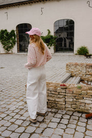 T-shirt rayé à manches longues rose porté par une femme, silhouette entière, casquette rose, pantalon blanc, de loin