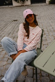 T-shirt rayé à manches longues rose porté par une femme, assise, jean clair, table