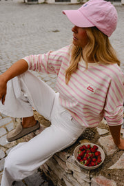 T-shirt rayé à manches longues rose porté par une femme, assise, casquette rose, pantalon blanc