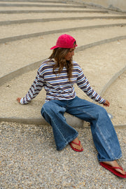 T-shirt rayé manches longues porté par une femme, assise, sur des gradins, casquette rose