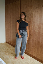 T-shirt moulant asymétrique noir porté par une femme, silhouette entière, sac à la main, vue de face