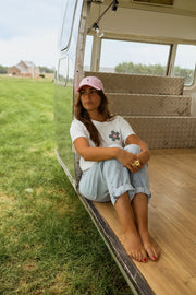 T-shirt à motif floral porté par une femme, assise, casquette rose, caravane