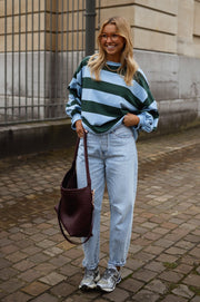 T-shirt ample à larges rayures porté par une femme, vue de face, pavés, sac bordeaux