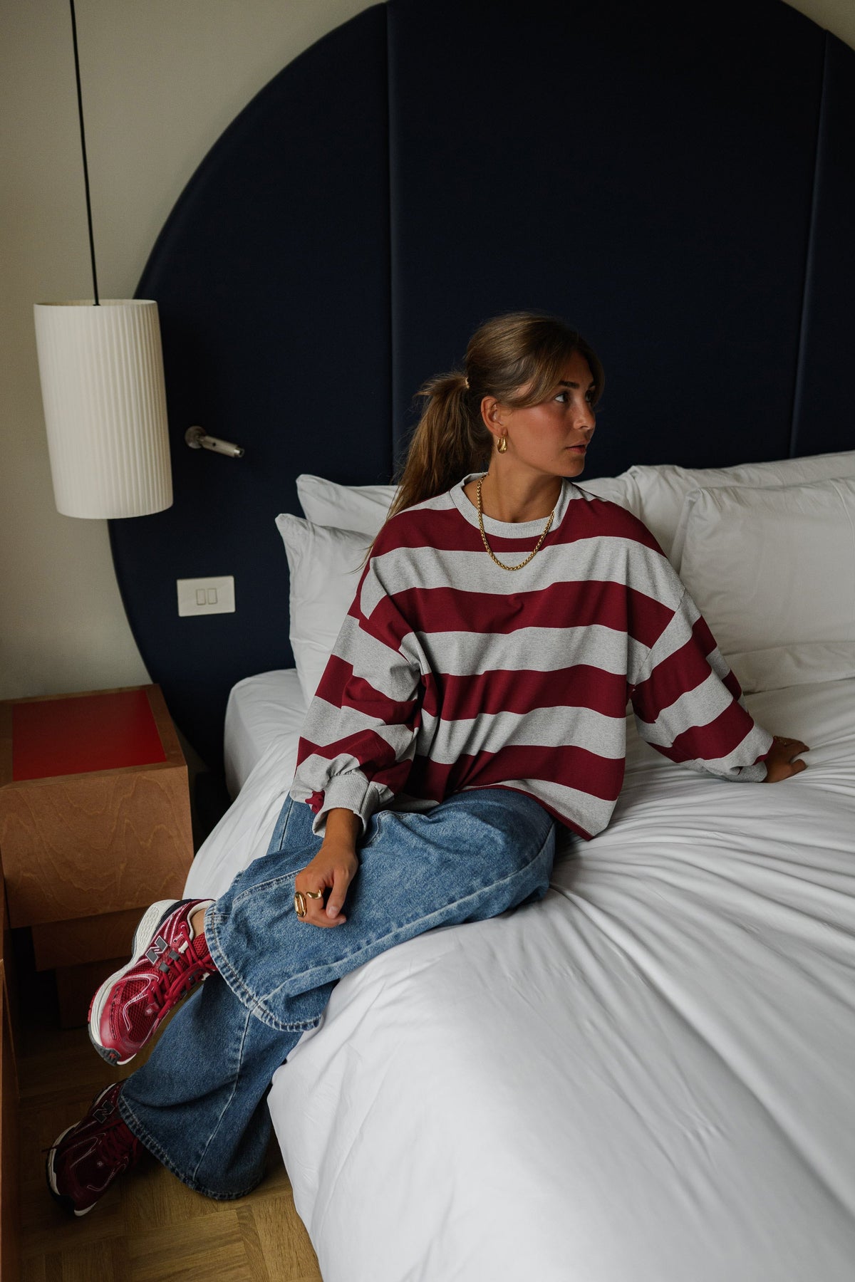 T-shirt rayé ample col rond porté par une femme, assise, sur un lit, regard de côté