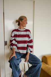 T-shirt rayé ample col rond porté par une femme, assise, sur un tabouret, mains sur les genoux