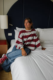 T-shirt rayé ample col rond porté par une femme, assise, sur un lit, vue de trois-quarts