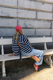 T-shirt rayé à dos ouvert porté par une femme, assise, sur un banc, casquette rose