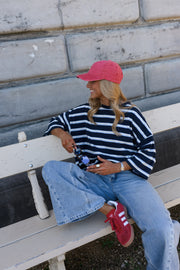 T-shirt rayé à dos ouvert porté par une femme, assise, sur un banc, casquette rose, de dos