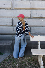 T-shirt rayé à dos ouvert porté par une femme, vue de dos, casquette rose, appuyée à un banc