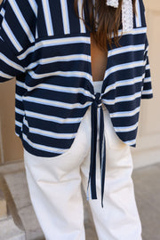 T-shirt rayé à dos ouvert porté par une femme, gros plan du dos ouvert et du nœud, pantalon blanc