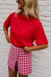 T-shirt ample à manches courtes rouge porté par une femme, vue rapprochée, jupe à carreaux