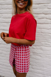 T-shirt ample à manches courtes rouge porté par une femme, vue rapprochée, jupe à carreaux, mains sur le t-shirt