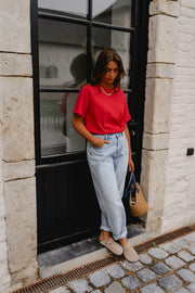 T-shirt ample à manches courtes rouge porté par une femme, silhouette entière, jean clair, devant une porte vitrée