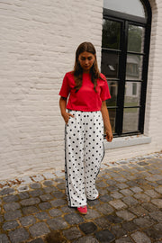 T-shirt ample à manches courtes rouge porté par une femme, silhouette entière, pantalon à pois, devant une fenêtre