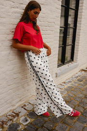 T-shirt ample à manches courtes rouge porté par une femme, vue de trois-quarts, pantalon à pois, adossée à un mur