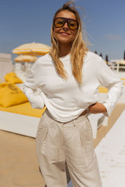 T-shirt doux à manches longues blanc porté par une femme, vue de face, lunettes de soleil, transats jaunes
