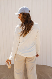 T-shirt doux à manches longues blanc porté par une femme, vue de trois-quarts, casquette blanche, cheveux longs