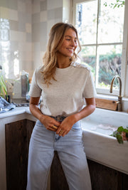T-shirt épais à boutons d’épaule porté par une femme, silhouette entière, mains dans les poches, sourire