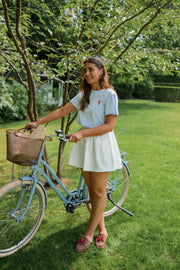 T-shirt homard brodé porté par une femme, silhouette entière, vélo, jupe blanche