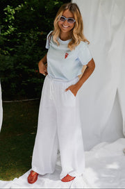 T-shirt homard brodé porté par une femme, vue de trois-quarts, pantalon blanc, mains dans les poches