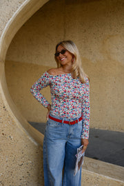 T-shirt fleuri asymétrique moulant porté par une femme, vue de trois-quarts, lunettes de soleil, ceinture rouge