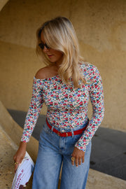 T-shirt fleuri asymétrique moulant porté par une femme, vue de trois-quarts, feuille à la main