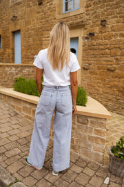 T-shirt blanc à logo vert porté par une femme, vue de dos, muret, jean large