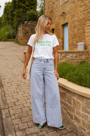 T-shirt blanc à logo vert porté par une femme, silhouette entière, muret, jean large