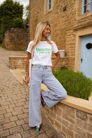 T-shirt blanc à logo vert porté par une femme, vue de trois-quarts, baskets, muret