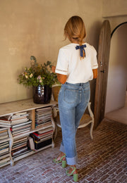 T-shirt épais brodé aux manches porté par une femme, vue de dos, nœud bleu dans les cheveux, jean