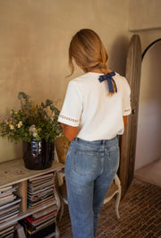 T-shirt épais brodé aux manches porté par une femme, vue de dos, ruban bleu dans les cheveux, jean