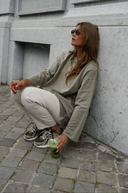 T-shirt loose à manches longues porté par une femme, assise, adossée à un mur, assise au sol, pantalon clair