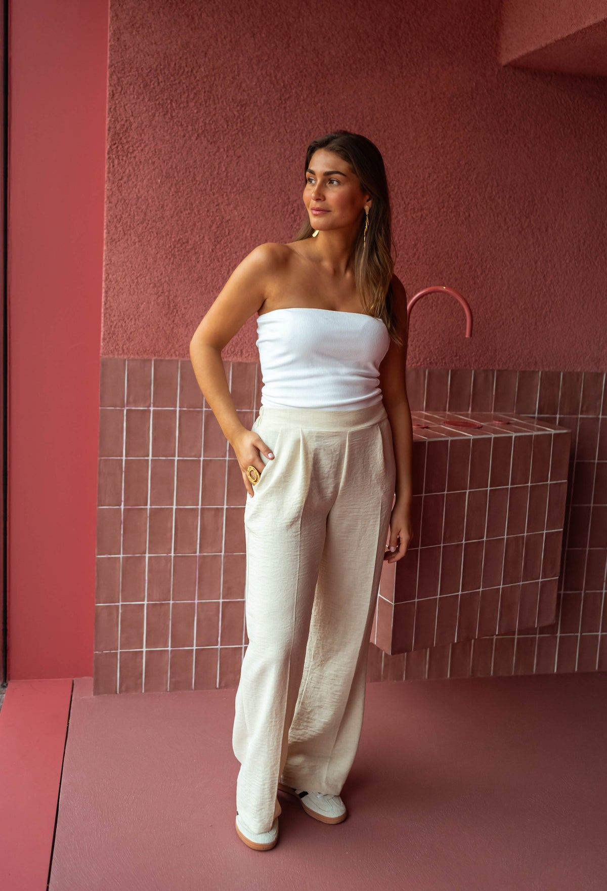Top élastiqué en matière t-shirt porté par une femme, silhouette entière, pantalon large beige, mur rose