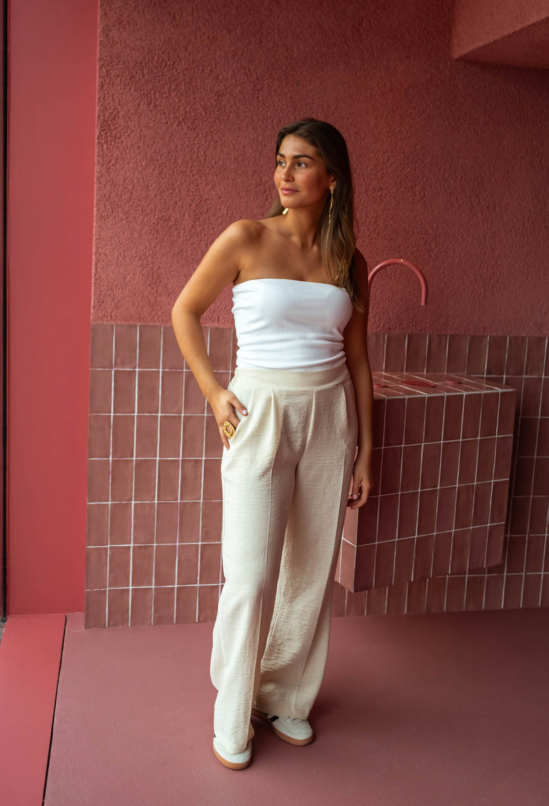 Top élastiqué en matière t-shirt porté par une femme, silhouette entière, pantalon large beige, mur rose