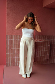Top élastiqué en matière t-shirt porté par une femme, silhouette entière, pantalon large beige, main dans les cheveux