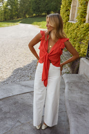 Top volanté à col V porté par une femme, silhouette entière, pantalon blanc, nœud