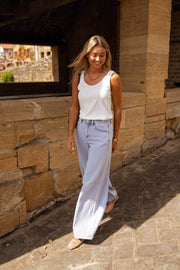 Top fluide effet lin blanc porté par une femme, silhouette entière, muret en pierre, jean bleu clair