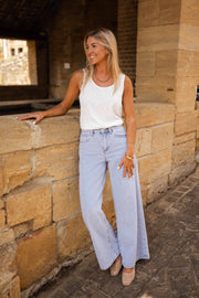 Top fluide effet lin blanc porté par une femme, silhouette entière, muret, pantalon large