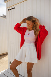 Top moulant col rond rose porté par une femme, silhouette entière, mur blanc, cardigan rouge
