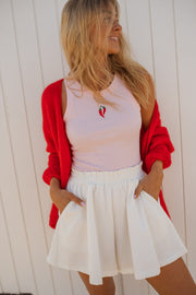 Top moulant col rond rose porté par une femme, vue de trois-quarts, cardigan rouge, short blanc