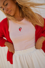 Top moulant col rond rose porté par une femme, vue rapprochée, cardigan rouge, cœur brodé