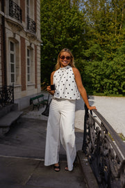 Top à pois effet ballon porté par une femme, silhouette entière, balustrade, pantalon blanc, de face