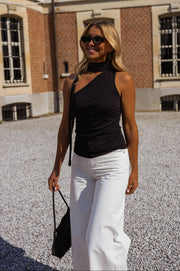 Top asymétrique moulant à nouer porté par une femme, silhouette entière, sac noir, pantalon blanc