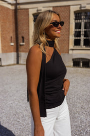 Top asymétrique moulant à nouer porté par une femme, vue de trois-quarts, foulard, pantalon blanc
