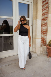 Top asymétrique moulant à nouer porté par une femme, silhouette entière, fenêtre, pantalon blanc
