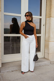 Top asymétrique moulant à nouer porté par une femme, silhouette entière, porte vitrée, pantalon blanc